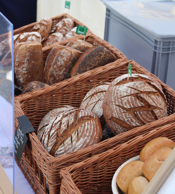 KI generiert: Brotlaibe in Körben auf einem Marktstand. Ein kleines Schild mit dem Text: "Langbrot Zwirbel 5 €".