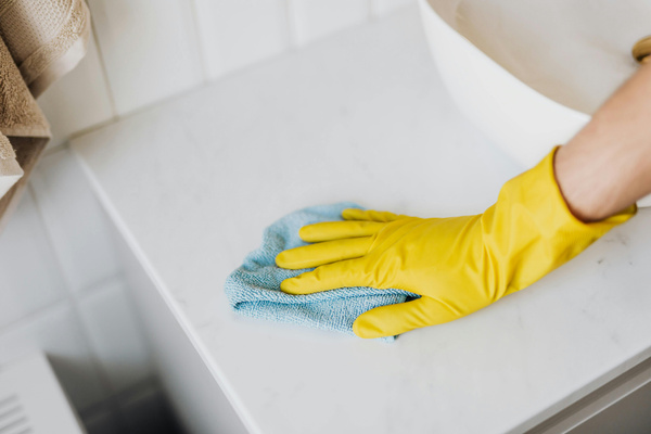 KI generiert: Eine Person reinigt mit gelbem Gummihandschuh und blauem Tuch eine weiße Oberfläche.