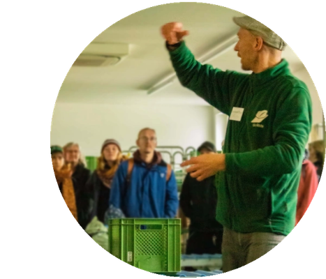 KI generiert: Eine Person spricht vor einer Gruppe Menschen in einem Raum; eine grüne Kiste steht im Vordergrund.