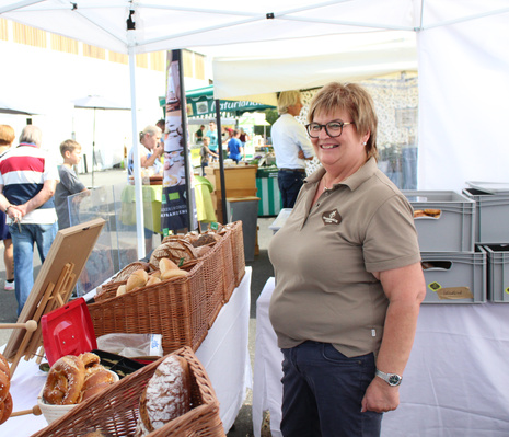 KI generiert: Eine Frau an einem Brotwarenstand auf einem Markt, lächelnd und freundlich.