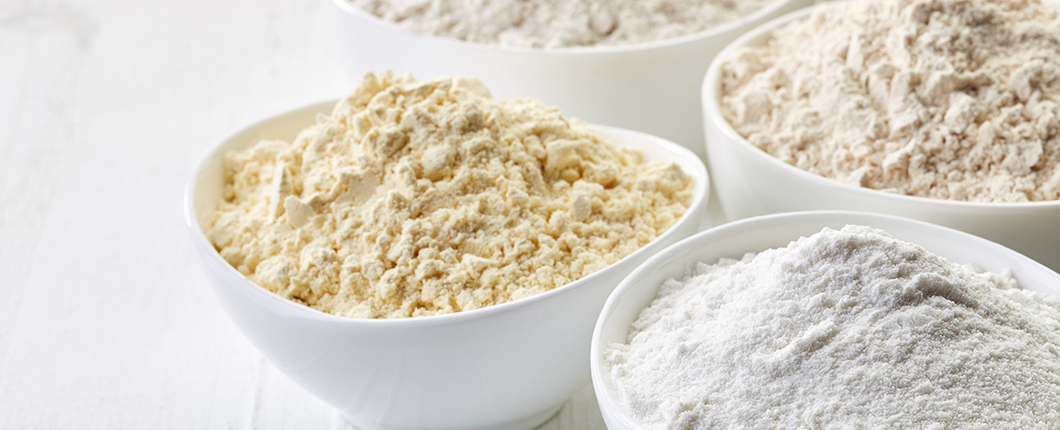 KI generiert: Verschiedene Mehlsorten in weißen Schalen auf weißem Hintergrund.