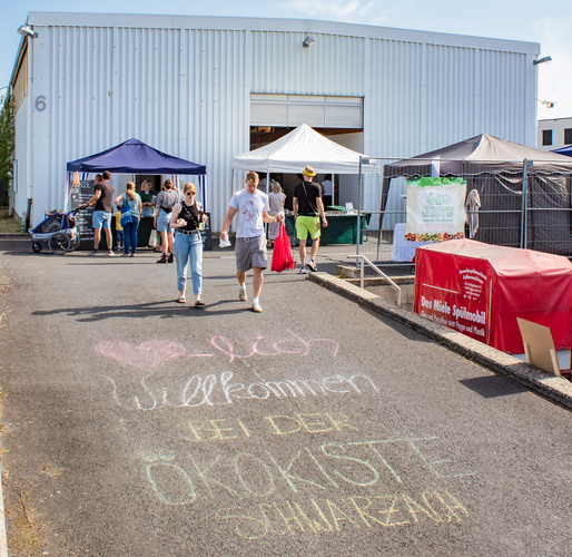 KI generiert: Ein Gebäude mit Ständen; Vorn Schrift: "Herzlich Willkommen bei der Ökokiste Schwaben."
