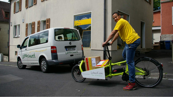 KI generiert: Ein Mann mit Lastenrad und Lieferwagen unterwegs. Text: "Lebenswursts" auf beiden Fahrzeugen.