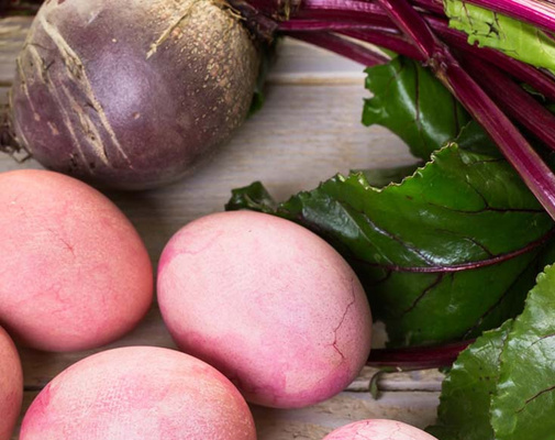 KI generiert: Rote Beete und rosafarbene Eier auf einem Holztisch mit roten Blättern.