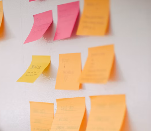 KI generiert: Post-its in Pink und Orange an einer Wand, einige mit Text beschriftet.