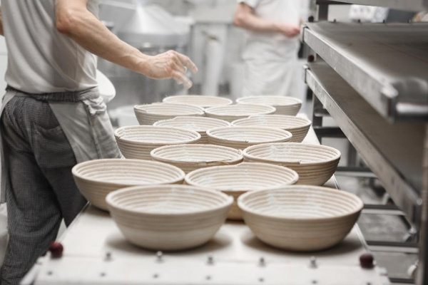 KI generiert: Bäckerei-Arbeiter formen Teig in Gärkörben. Keine sichtbaren Textelemente.