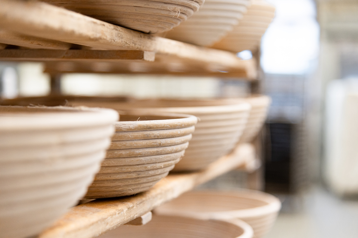 KI generiert: Mehrere runde Gärkorbe aus Rattan auf Regalen in einer Bäckerei.