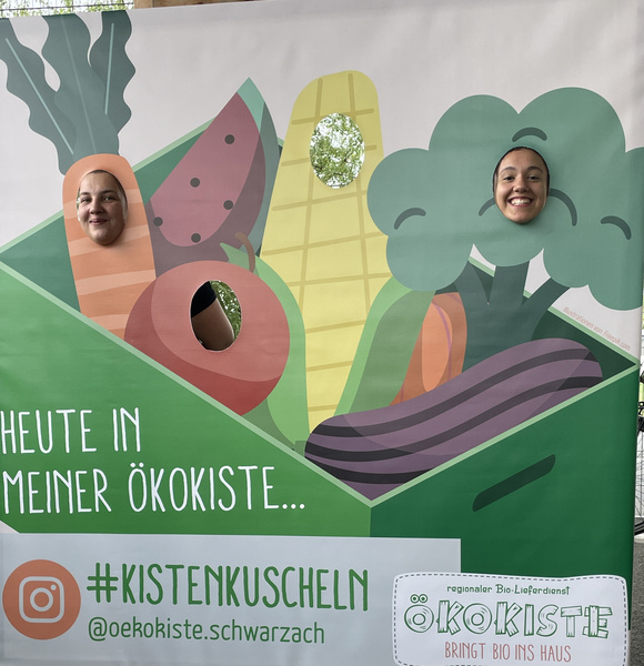 KI generiert: Zwei Personen stecken ihre Köpfe durch Aussparungen in einem Pappbild mit Gemüsemotiven.

Text: Heute in meiner Ökokiste... #Kistenkuscheln @oekokiste.schwarzach