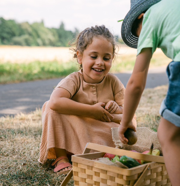 KI generiert: Zwei Kinder beim Picknick im Freien mit Korb voller Obst.