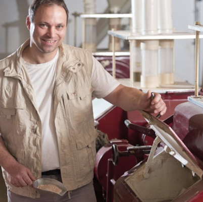 KI generiert: Ein Mann steht neben einer Maschine und hält eine Schaufel mit Körnern oder Mehl.