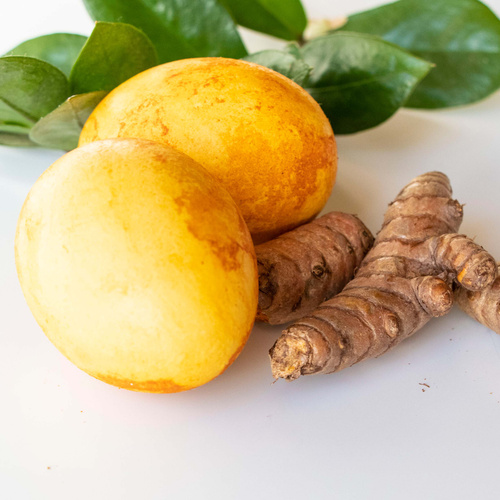 KI generiert: Frische Gelbwurzknollen und gelbe Früchte mit grünen Blättern auf weißem Hintergrund.