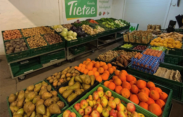 KI generiert: Marktstand mit frischem Obst und Gemüse. Text: "Familie Tietze, regional, bio-logisch".
