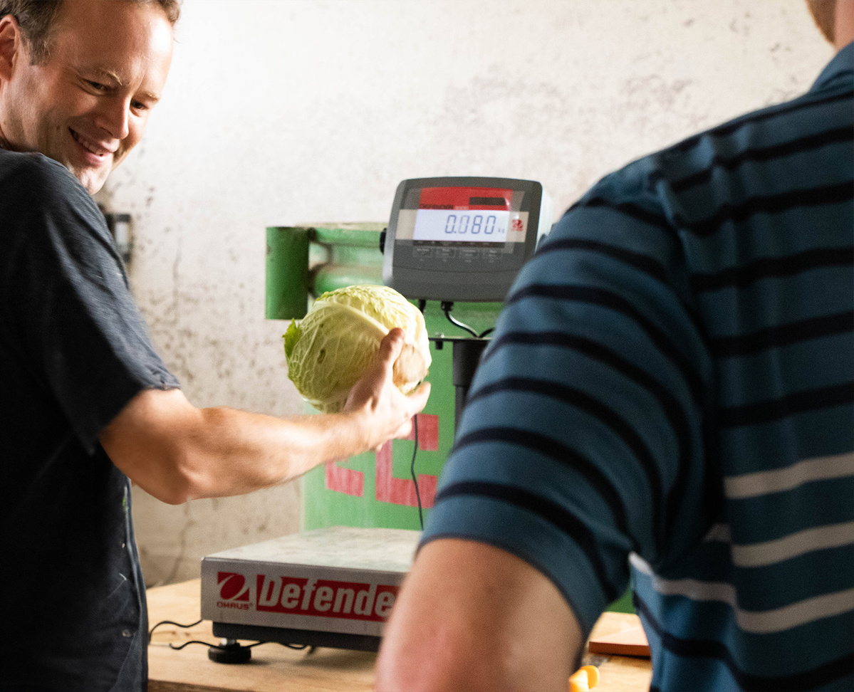 KI generiert: Ein Mann wiegt Gemüse, Kohl auf einer elektronischen Waage. Text: "0.080" auf dem Display.
