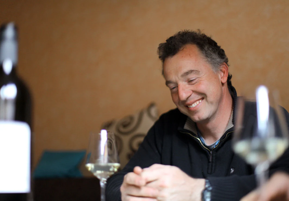 KI generiert: Ein lächelnder Mann sitzt an einem Tisch mit Weingläsern und einer Flasche.